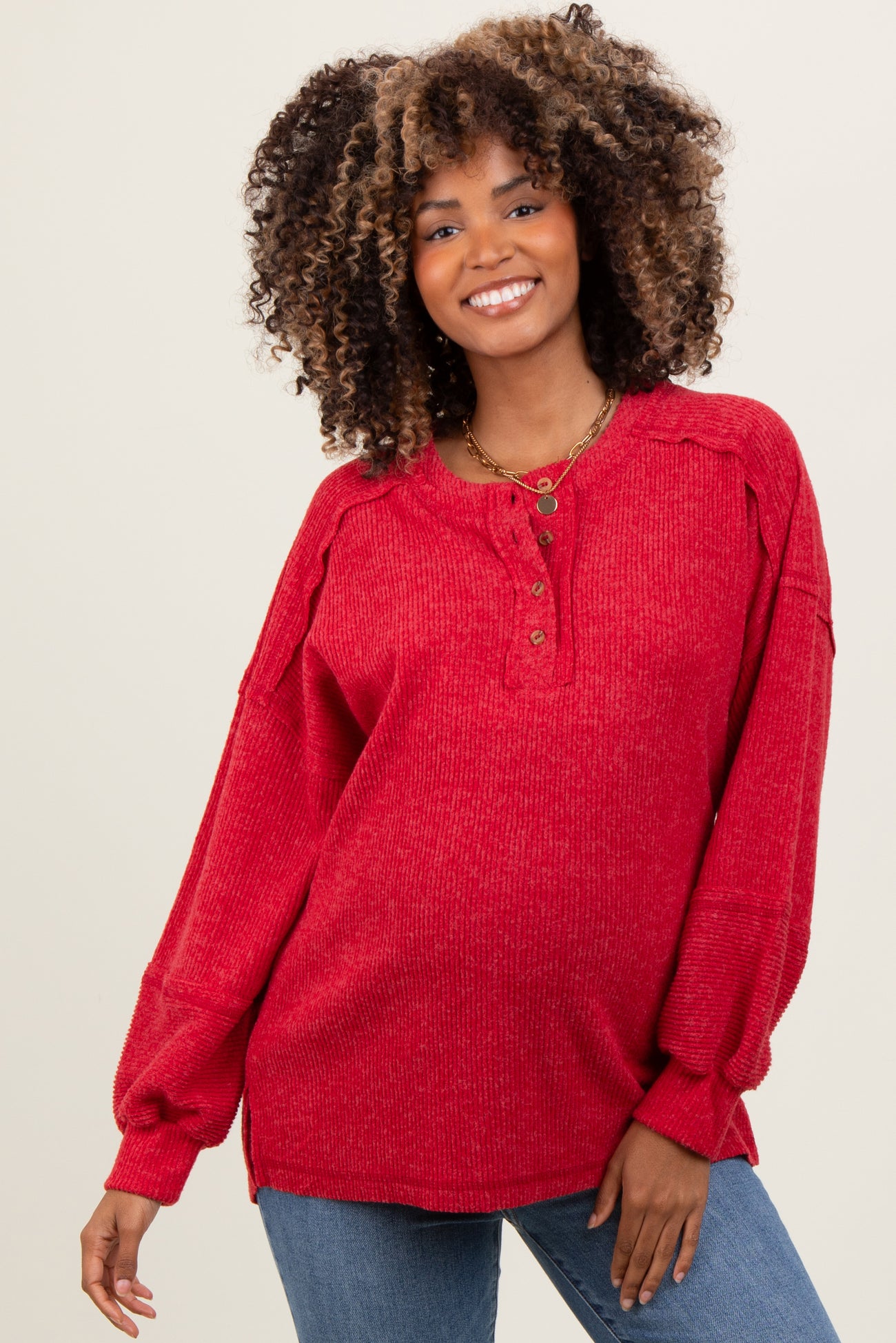woman wearing a red long sleeve maternity top with button details and relaxed fit, smiling while showing her baby bump