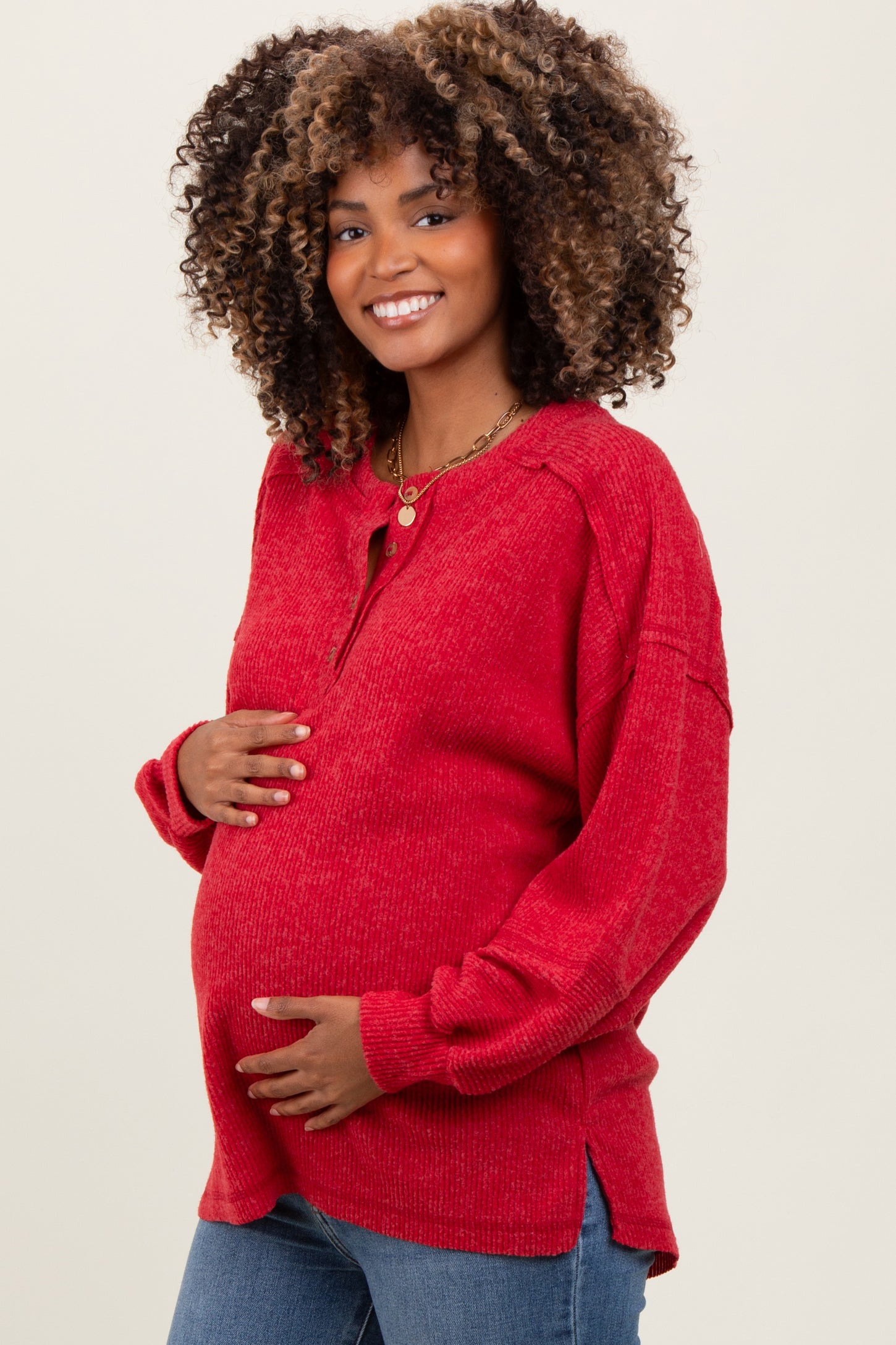 woman wearing a red maternity long sleeve sweater, smiling and holding her baby bump