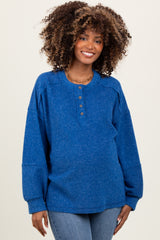 woman wearing a blue ribbed maternity top with button details and long sleeves, smiling at the camera