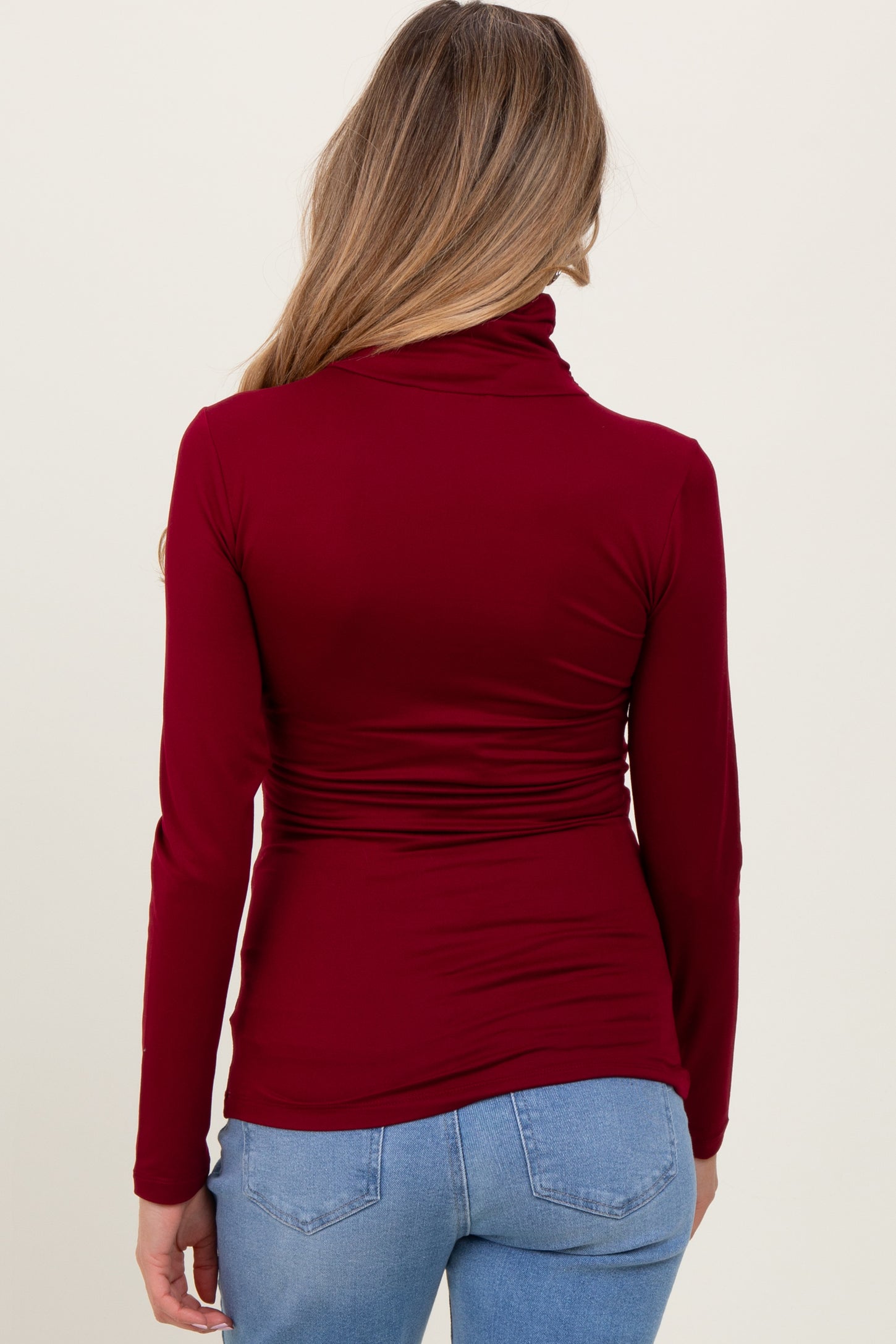 woman wearing a burgundy long sleeve maternity top with a cowl neck and gathered detailing at the waist