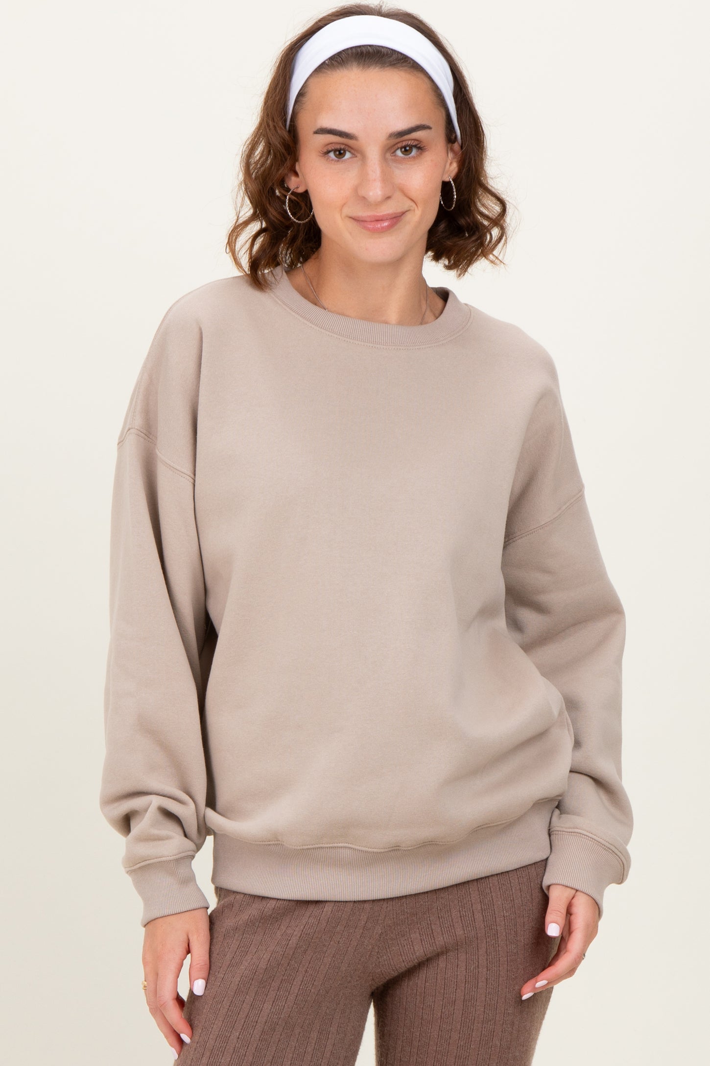 woman wearing a beige oversized sweatshirt with dropped shoulders and a round neckline, paired with brown ribbed pants