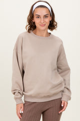 woman wearing a beige oversized sweatshirt with dropped shoulders and a round neckline, paired with brown ribbed pants
