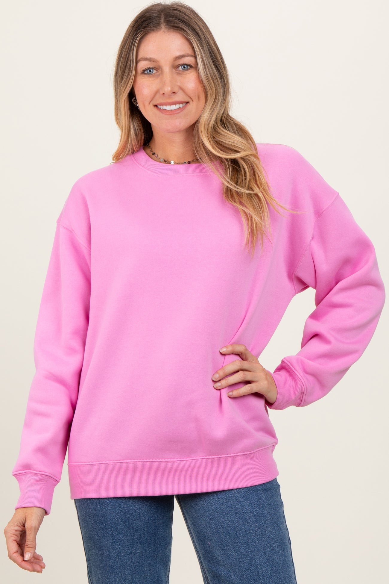 woman wearing a bright pink oversized sweatshirt with long sleeves and a crew neckline, paired with denim jeans