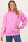 woman wearing a bright pink oversized sweatshirt with long sleeves and a crew neckline, paired with denim jeans