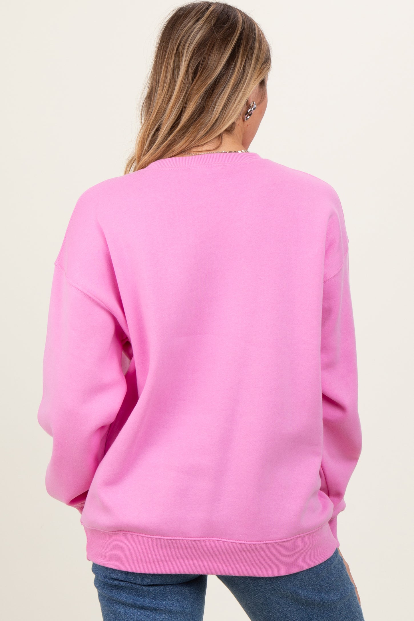 woman wearing a bright pink oversized sweatshirt, showing the back view, styled with blue jeans