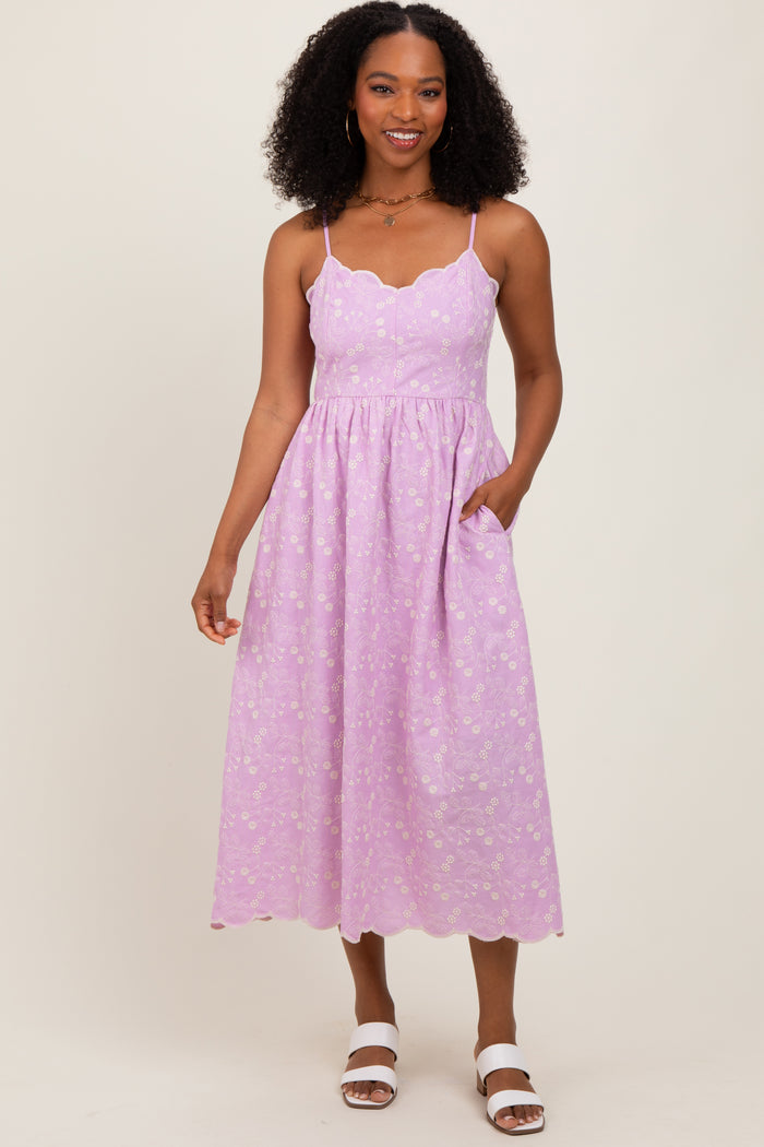 woman wearing a lavender midi dress with scalloped neckline and floral patterns, featuring pockets and spaghetti straps