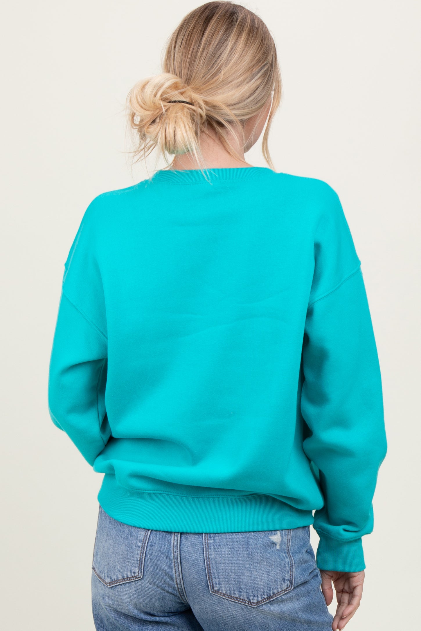 woman wearing a vibrant teal oversized sweatshirt with a relaxed fit, viewed from the back