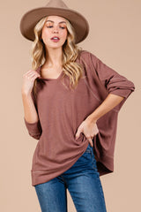 woman wearing a oversized mauve long sleeve sweater with a v-neck and distressed jeans, accessorized with a wide-brim hat