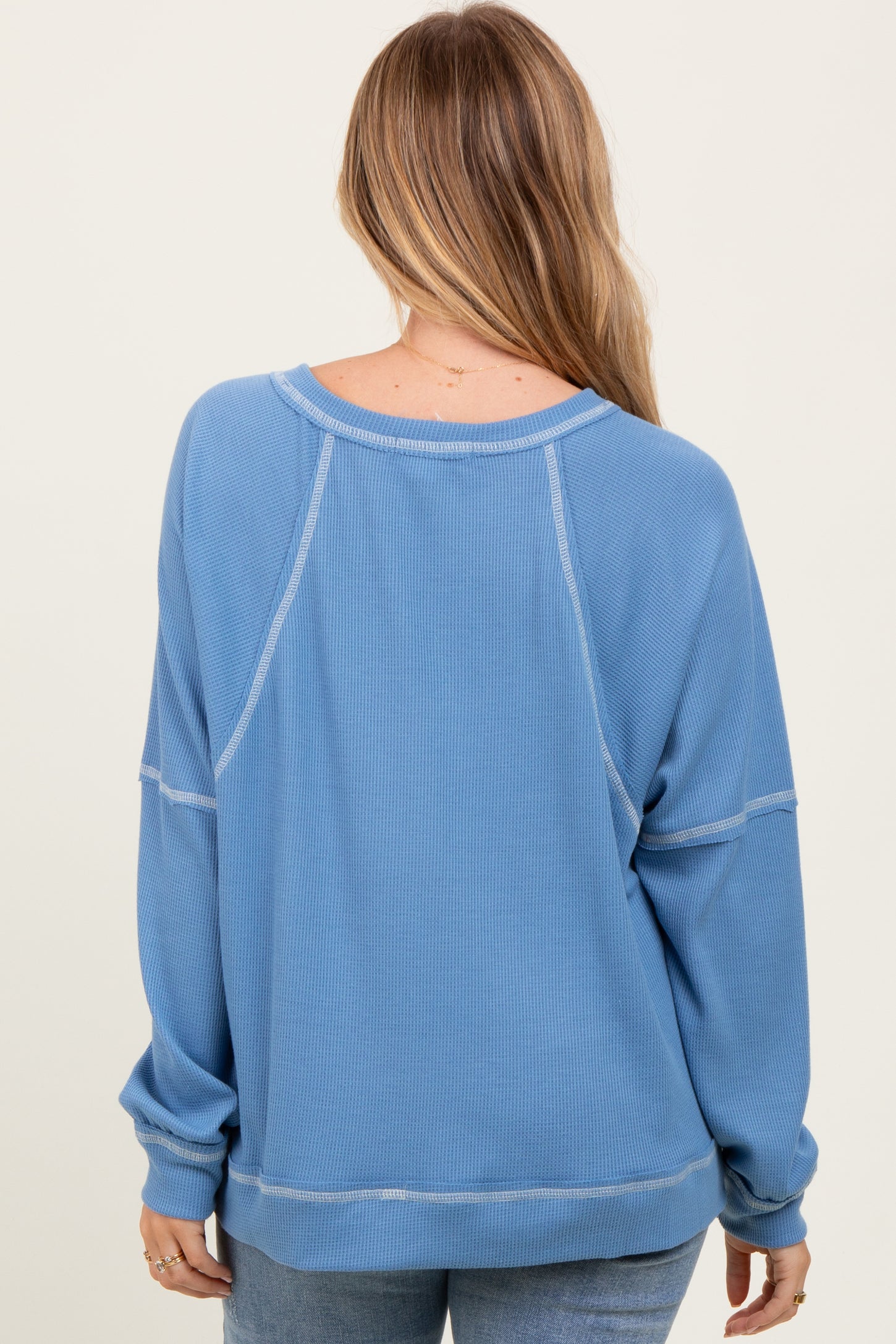 woman wearing a blue oversized waffle knit sweatshirt with a relaxed fit and raglan sleeves