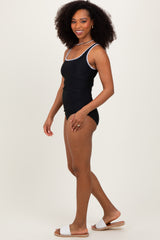 woman wearing a black swimsuit with white trim, posing sideways with curly hair and sandals
