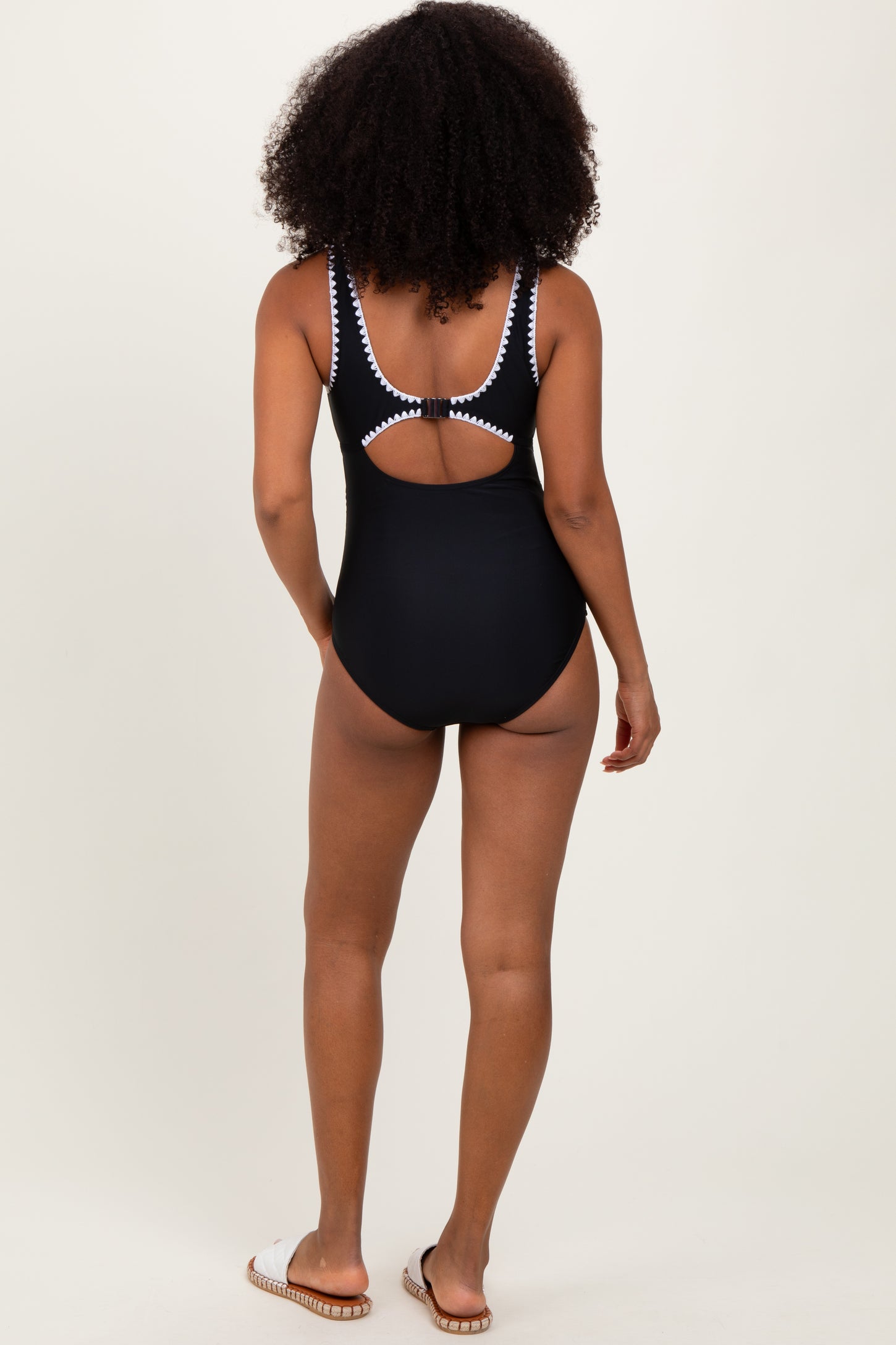 woman wearing a black one-piece swimsuit with a white trim and a cut-out back, positioned with her back to the camera