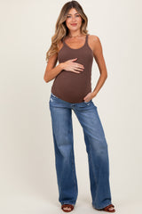 woman wearing a brown ribbed maternity tank top and distressed blue flared jeans, holding her baby bump