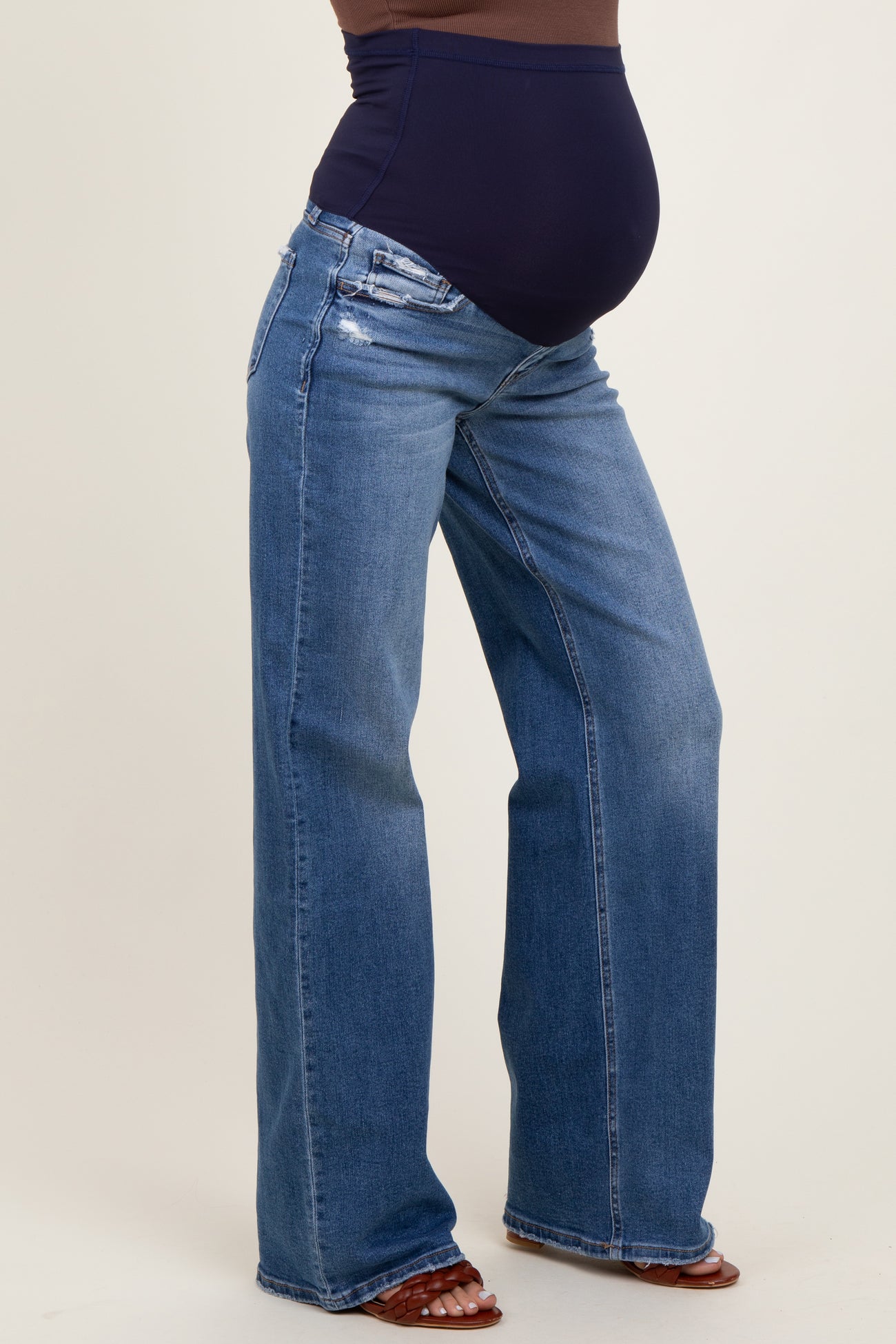 woman wearing dark blue maternity jeans with a high waistband and distressed details, showing her baby bump