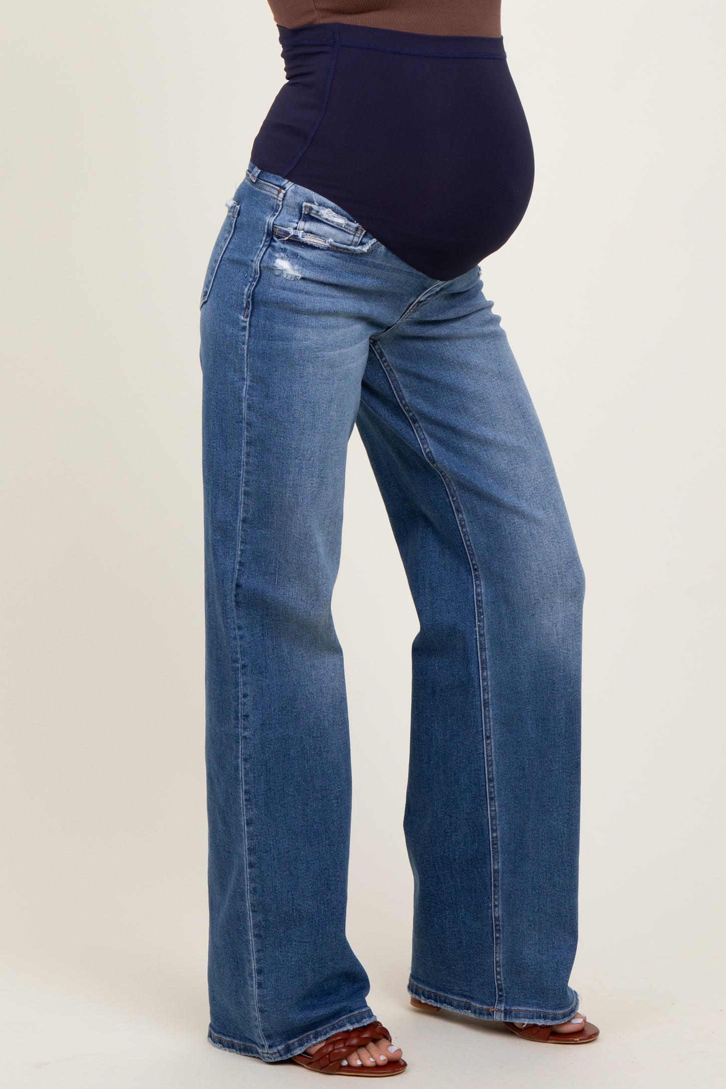 woman wearing dark blue maternity jeans with a high waistband and distressed details, showing her baby bump