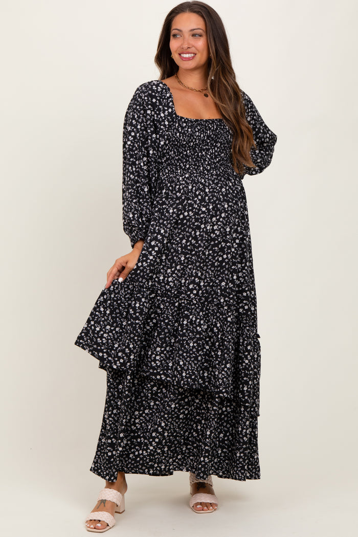 woman wearing a black floral maternity maxi dress with long sleeves and a tiered skirt, showing her baby bump