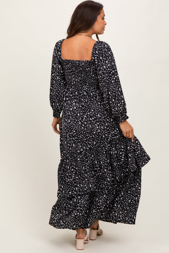 woman wearing a black floral maternity maxi dress with long sleeves and a ruffled hem, showing a baby bump