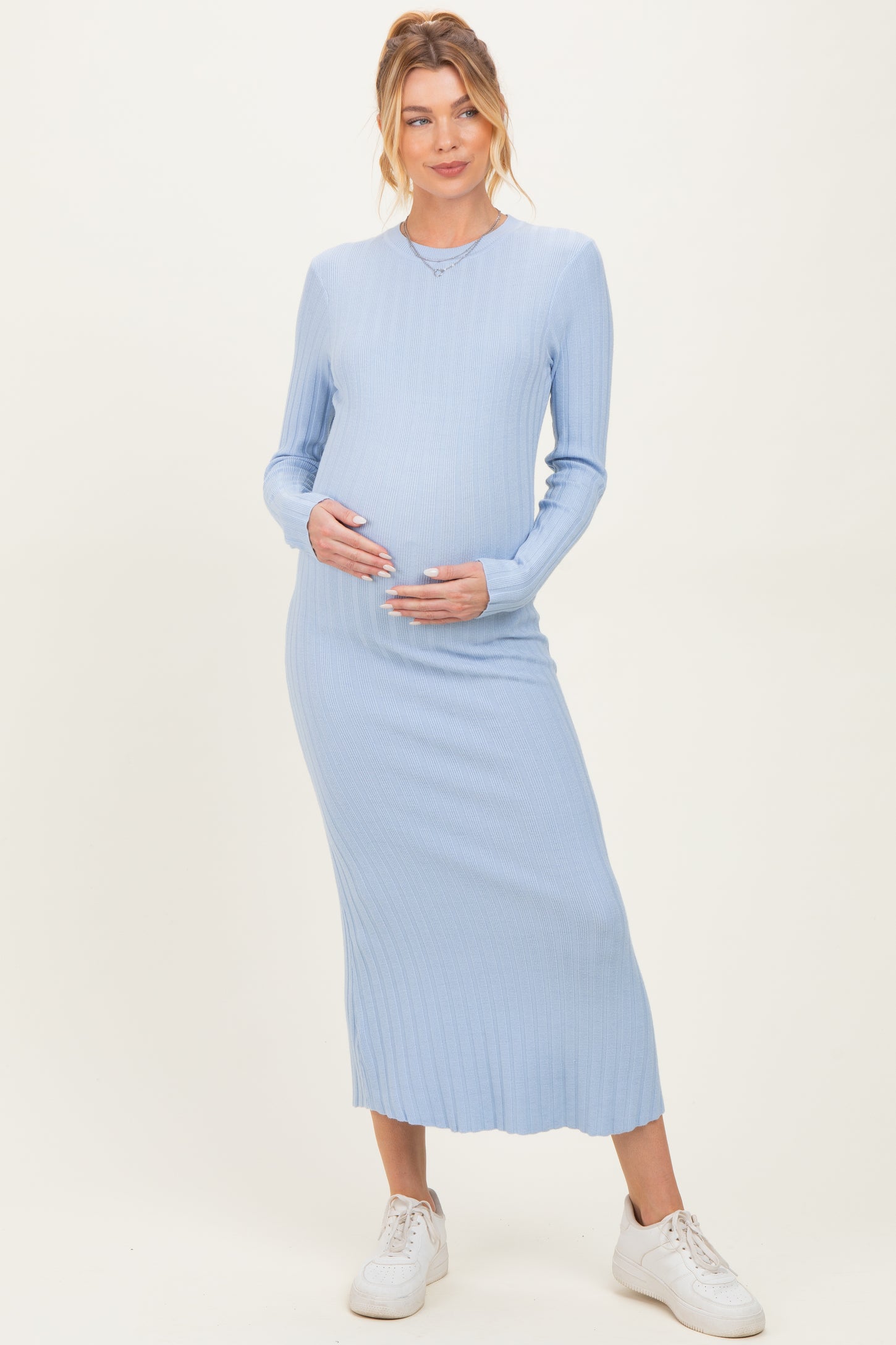 woman wearing a light blue ribbed maternity dress with long sleeves and a visible baby bump, holding her belly