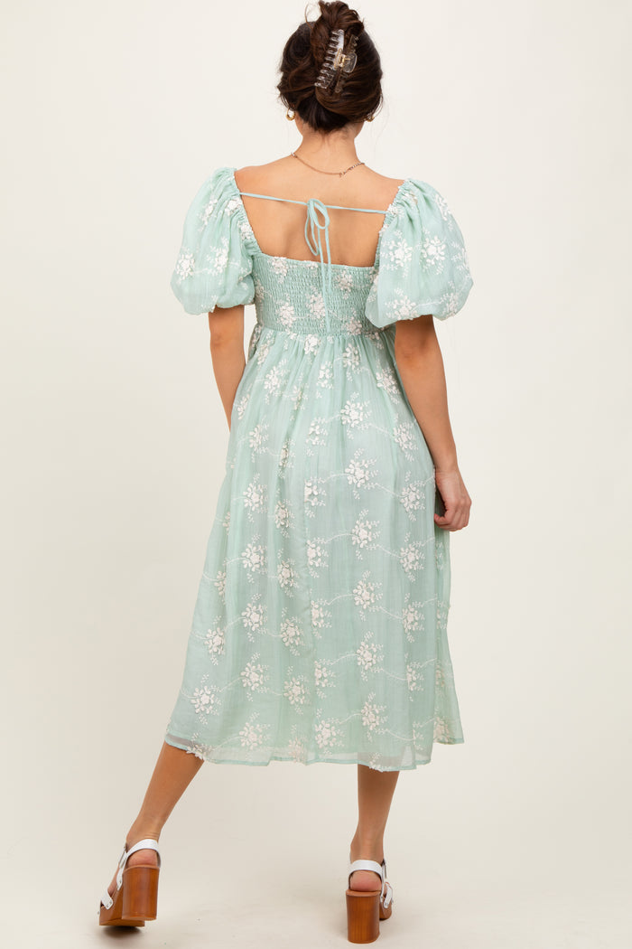 woman wearing a mint green puff sleeve dress with floral embroidery and a tied back detail