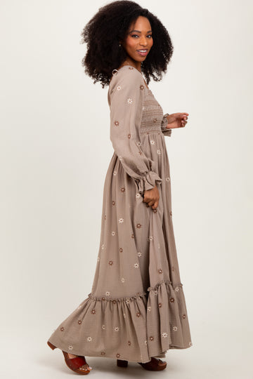 woman wearing a brown floral embroidered maxi dress with long sleeves and a ruffled hem