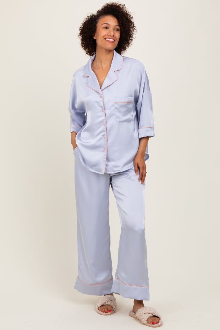 woman wearing a light blue satin pajama set with contrasting pink piping and loose-fitting pants