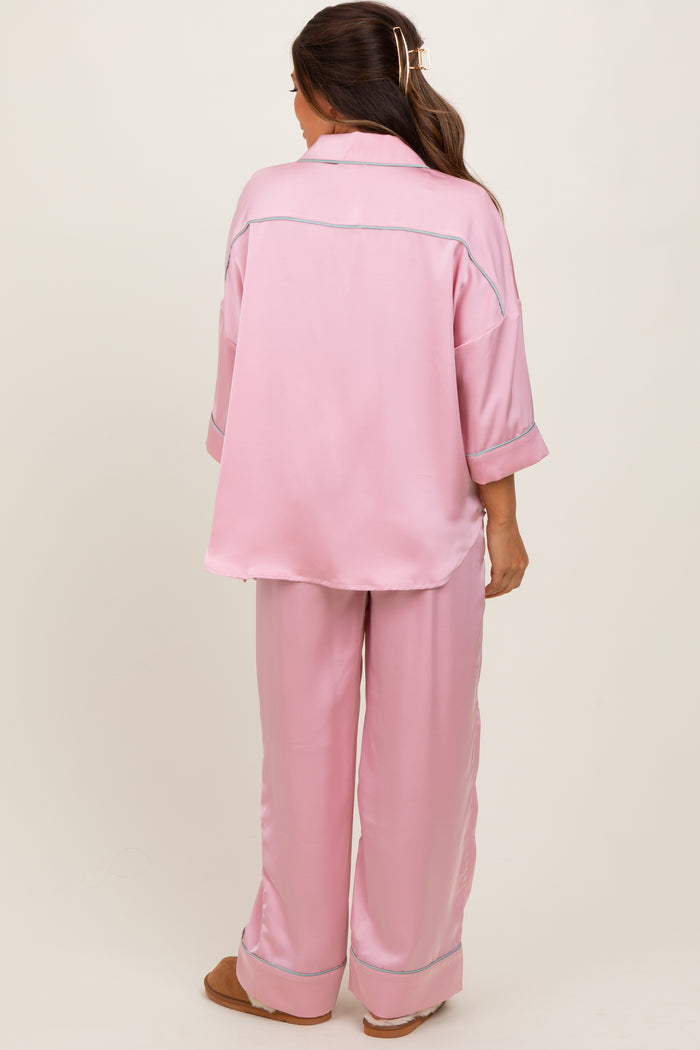 woman wearing a pink satin maternity pajama set with a relaxed fit and contrast piping, viewed from the back