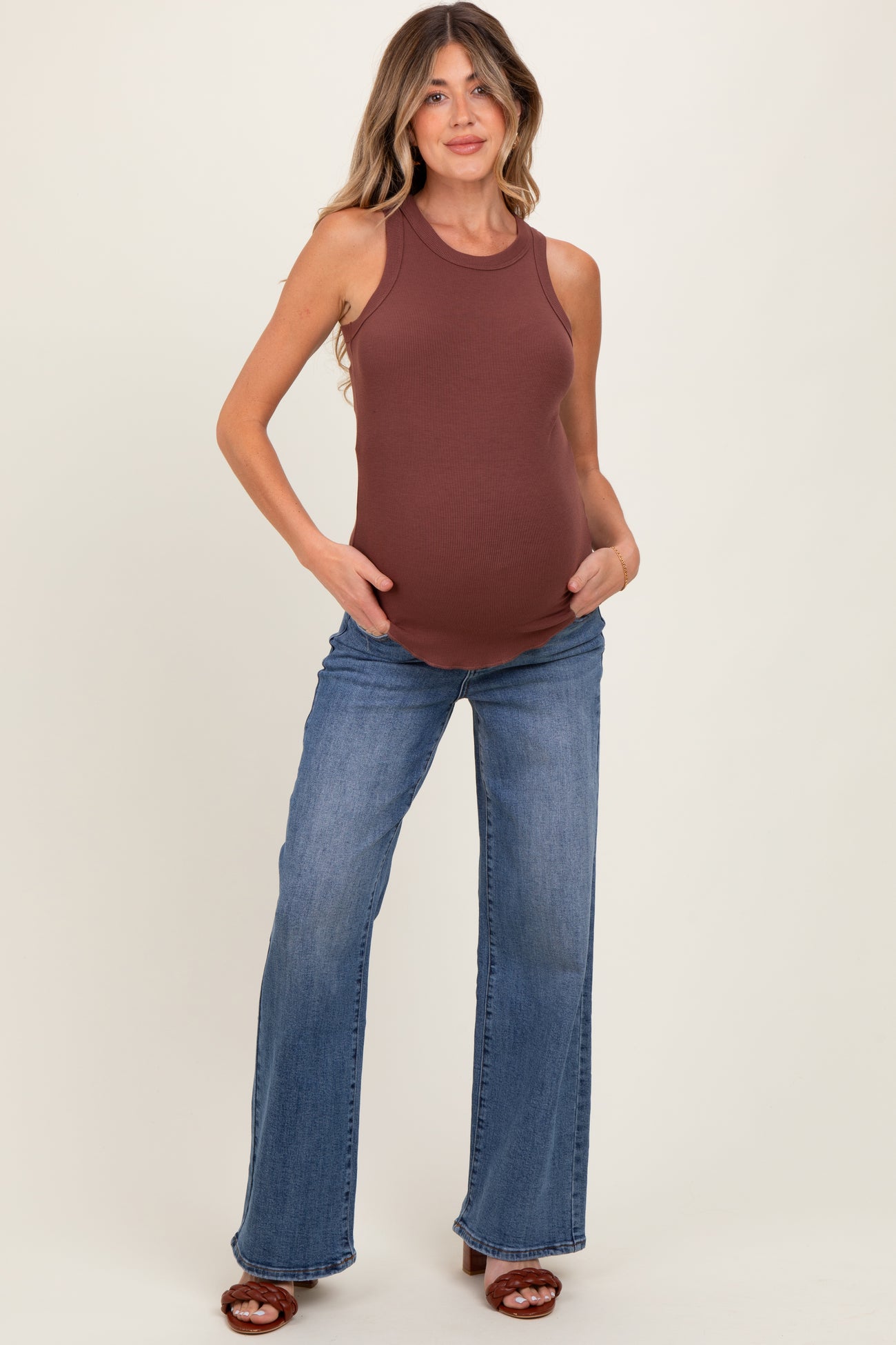 woman wearing a brown ribbed maternity tank top and blue flared jeans, showcasing her baby bump