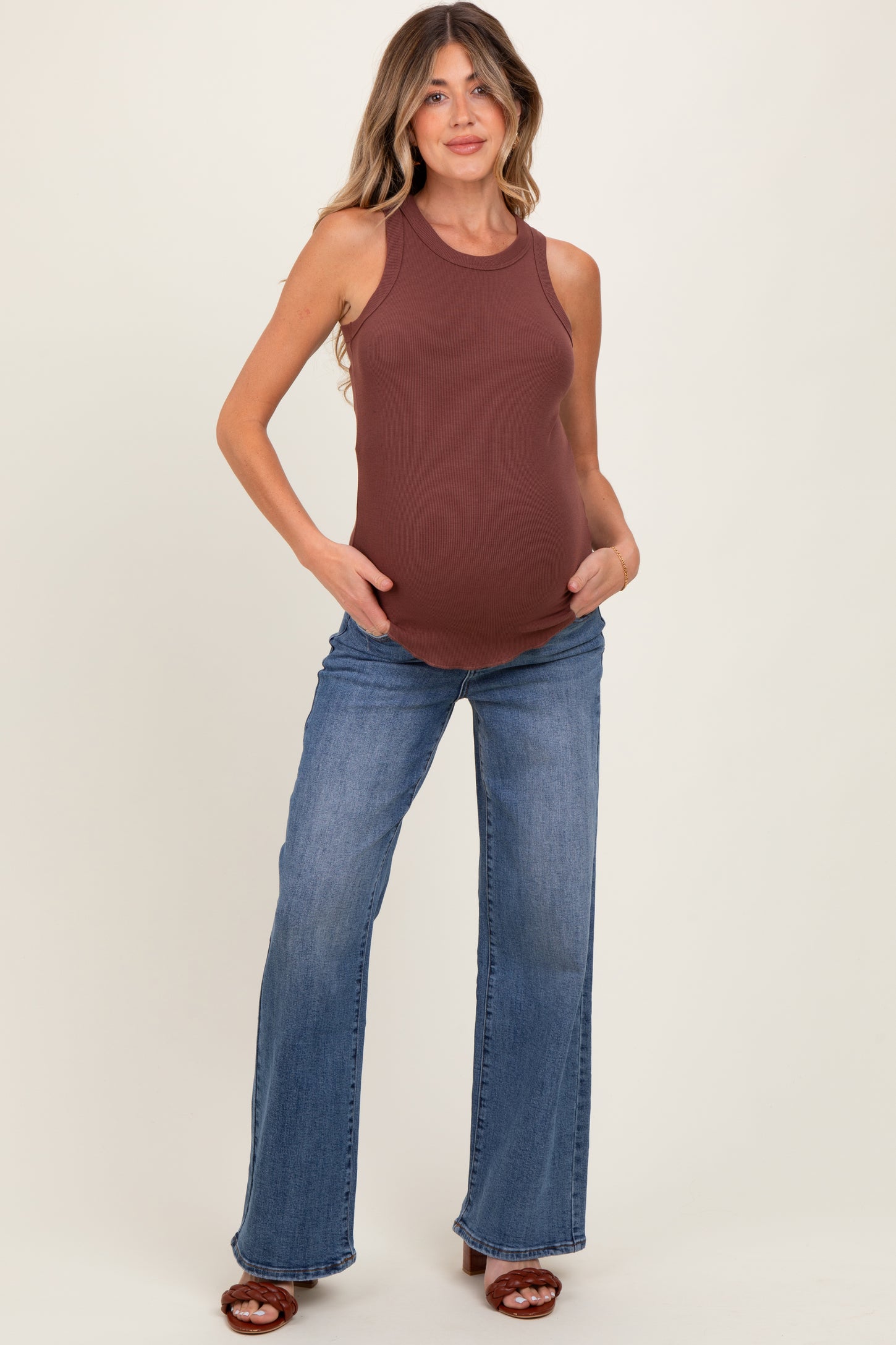 woman wearing a brown ribbed maternity tank top and blue flared jeans, showcasing her baby bump