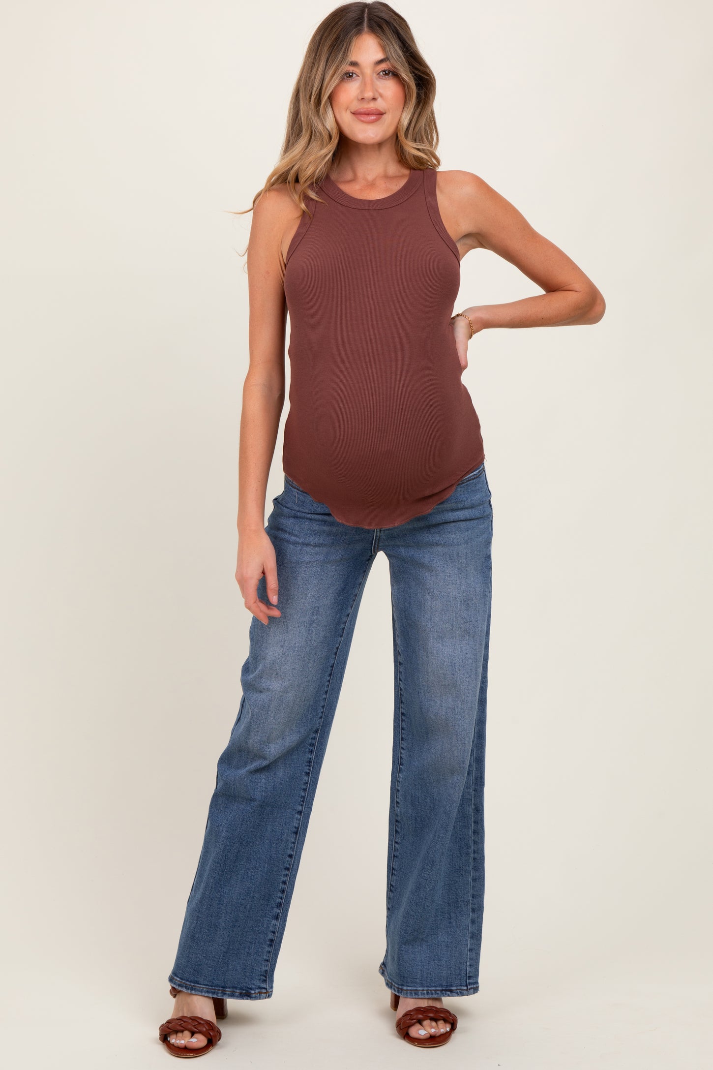 woman wearing a brown ribbed maternity tank top and blue flared jeans, showing her baby bump