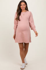 woman wearing a light pink maternity sweater dress with puff sleeves and a visible baby bump