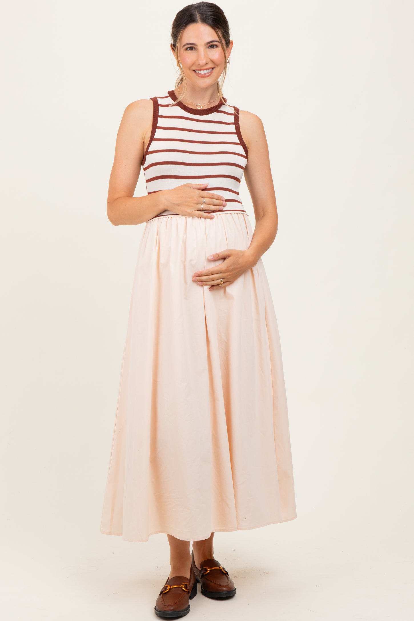 woman wearing a striped maternity tank top and a flowing midi skirt, cradling her baby bump