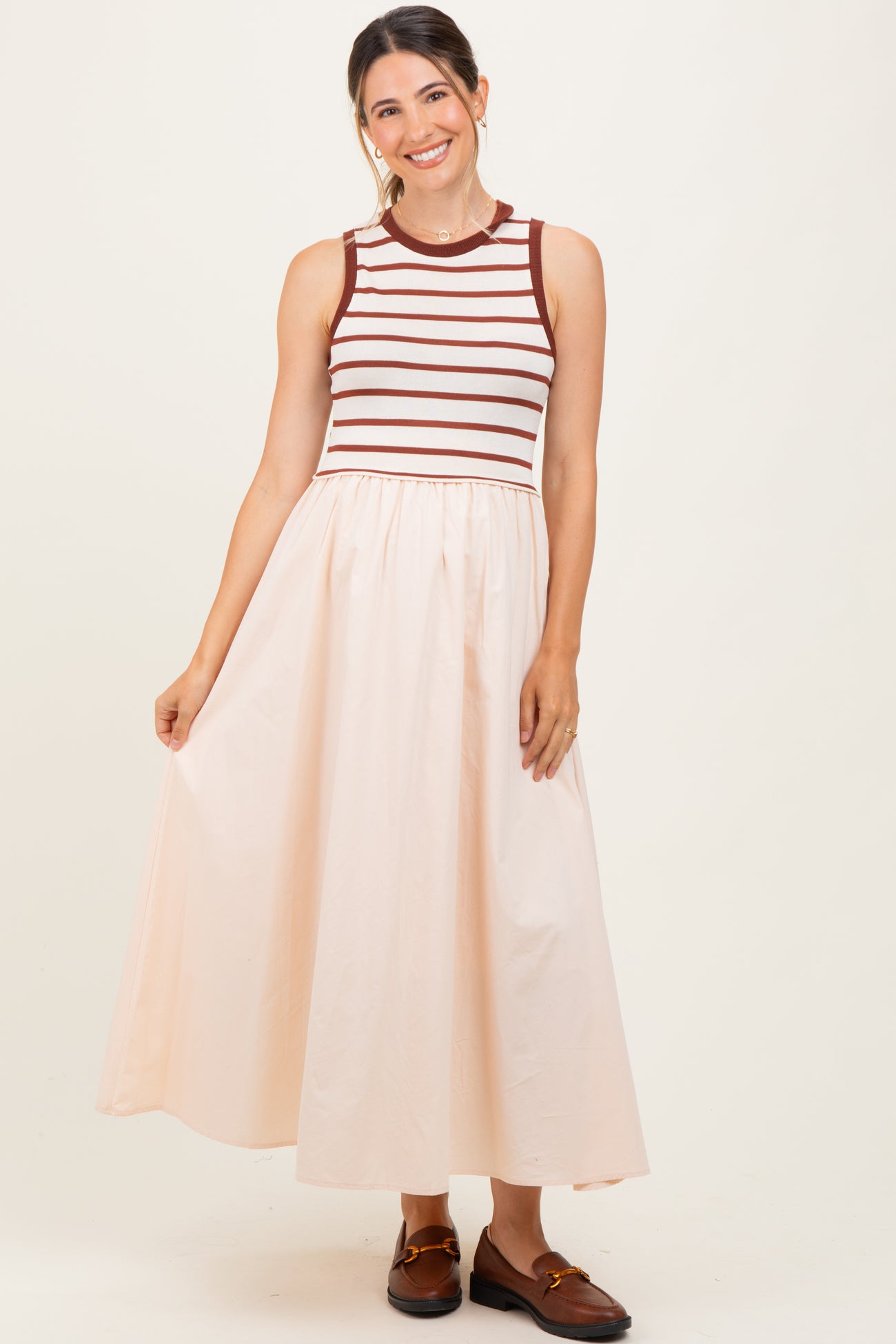 woman wearing a striped sleeveless maternity dress with a fitted top and a flowy peach skirt, smiling and posing