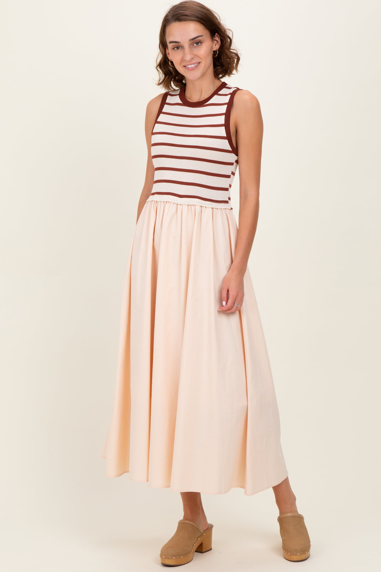 woman wearing a sleeveless striped bodice dress with a flowy peach skirt and brown clogs
