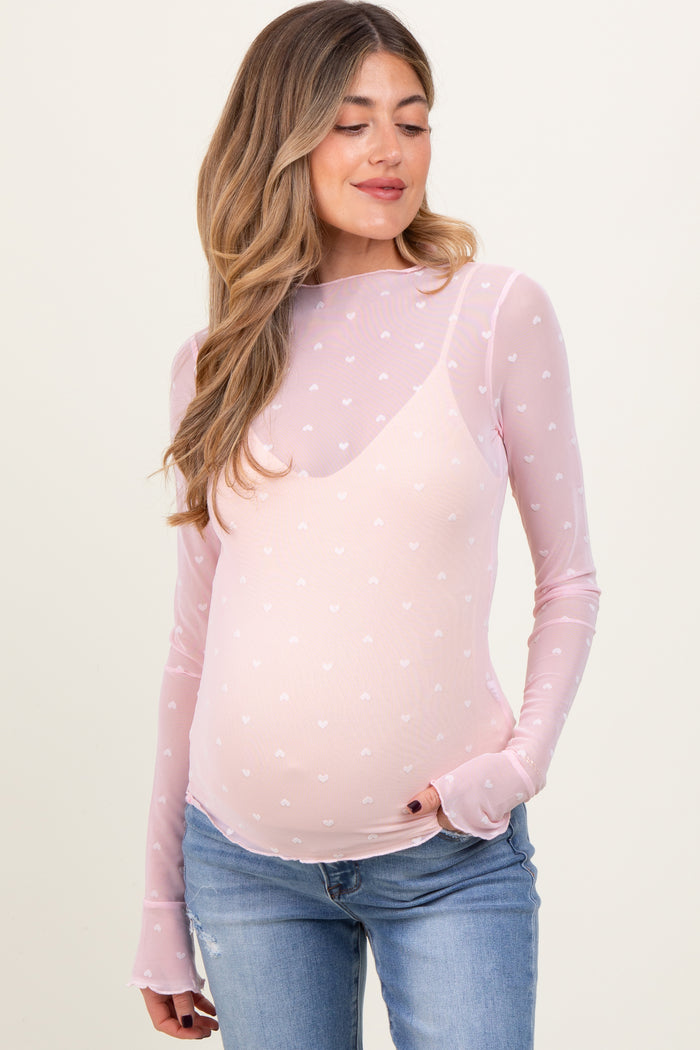 woman wearing a sheer pink maternity top with heart patterns and long sleeves, showing a baby bump