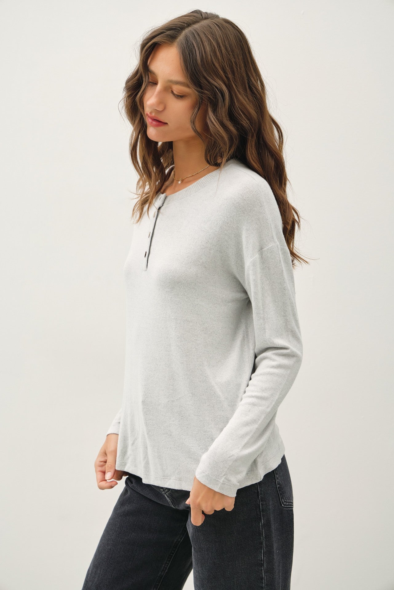 woman wearing a light gray long sleeve henley top with button details and casual black jeans