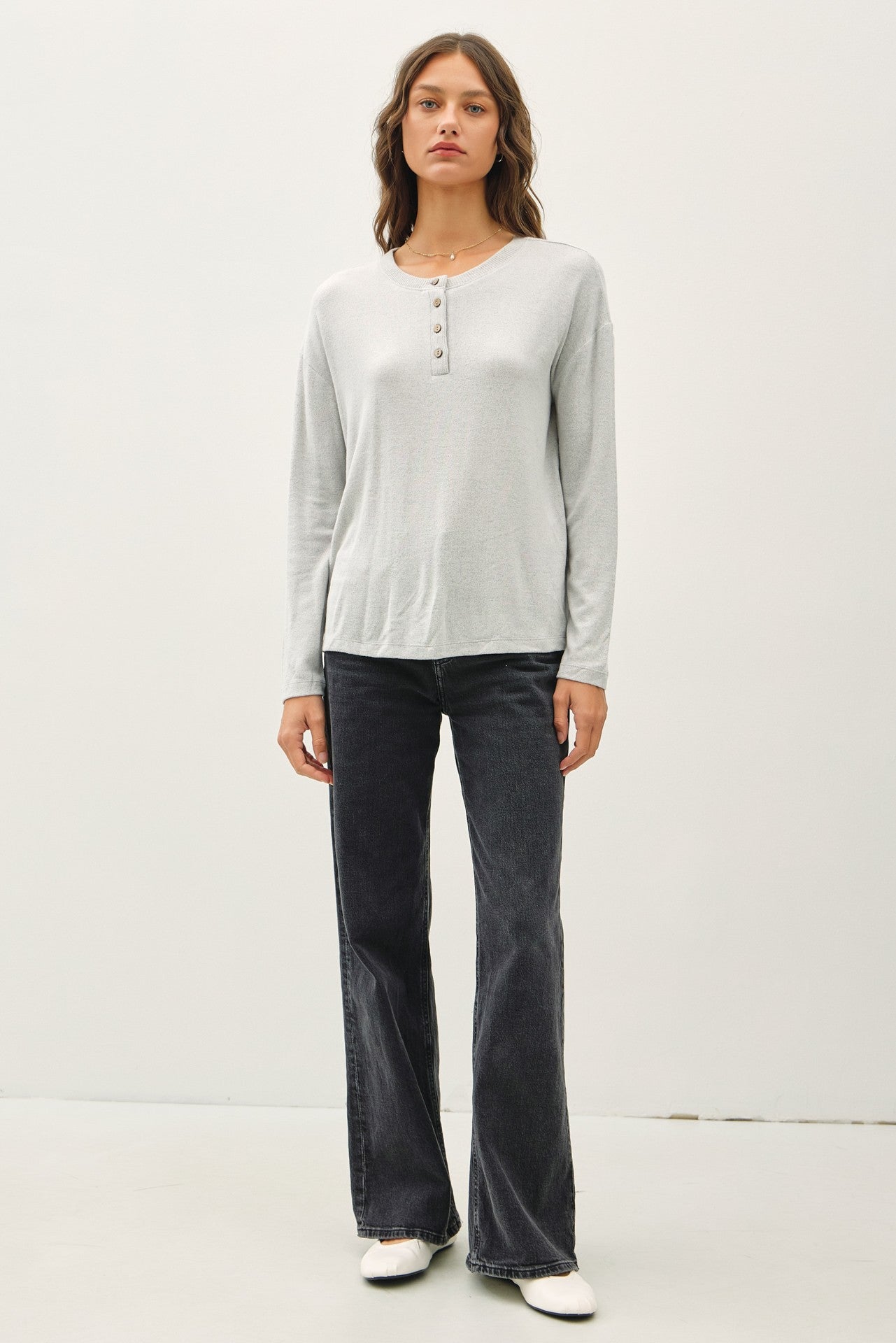 woman wearing a light gray long sleeve henley shirt and black flare jeans