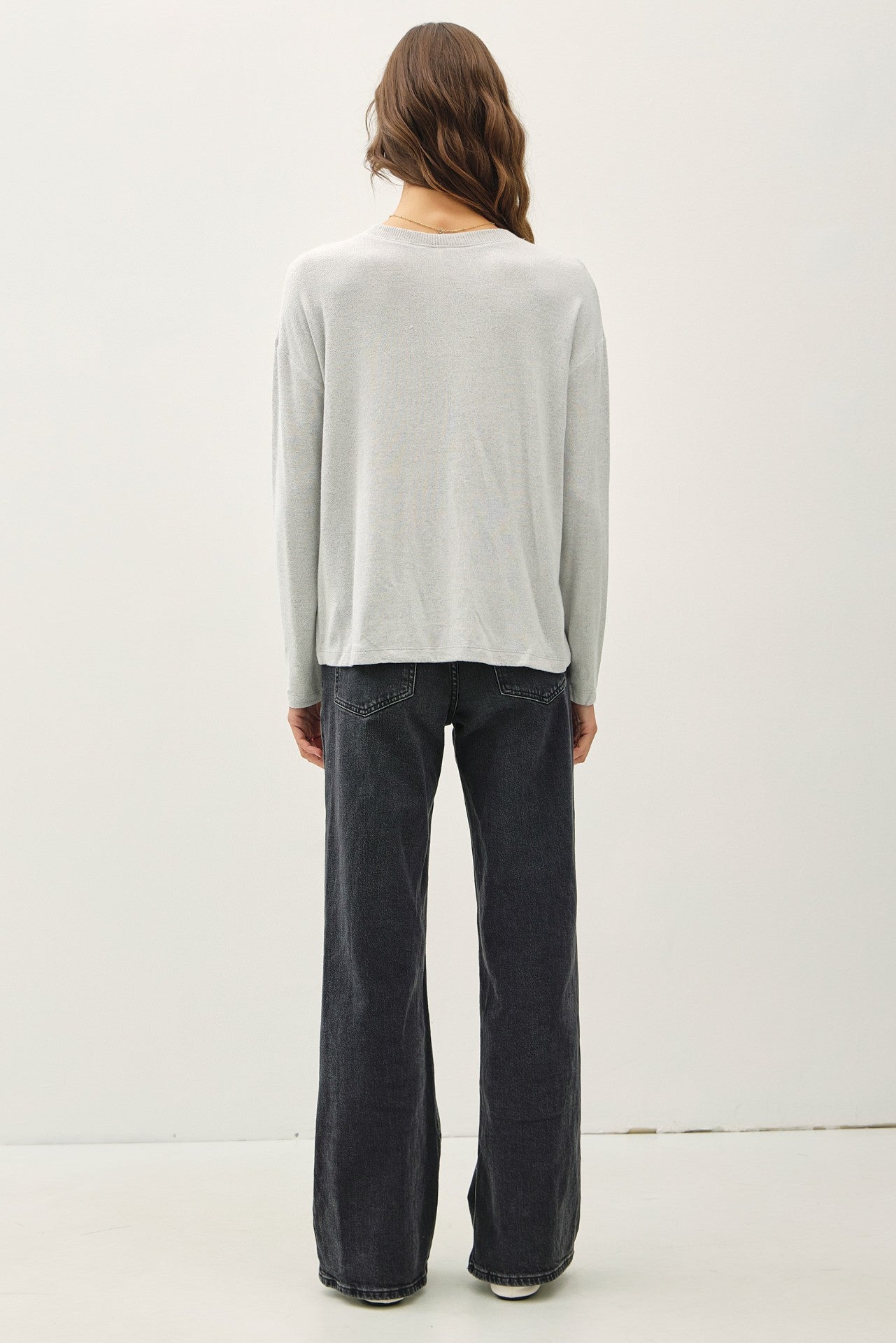 woman wearing a light gray long sleeve top and black wide-leg jeans, viewed from the back