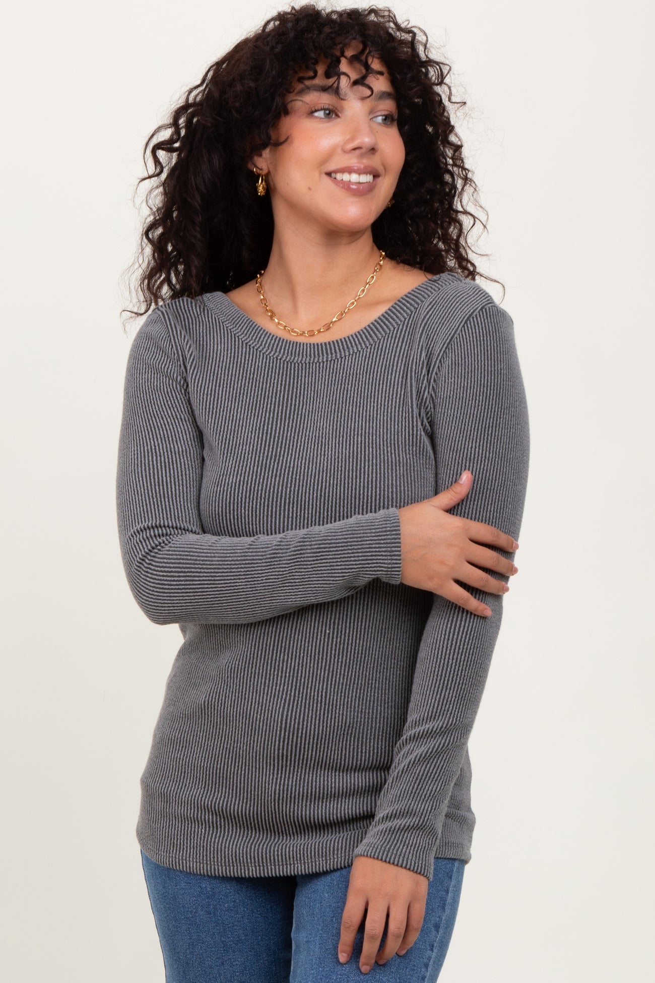 woman wearing a gray ribbed long sleeve top and smiling, with loose curls and gold earrings