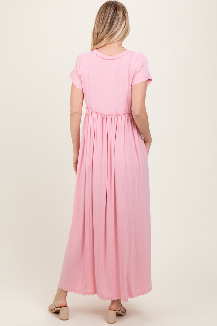 woman wearing a light pink short sleeve maxi dress with an elastic waistband and side pockets, viewed from the back