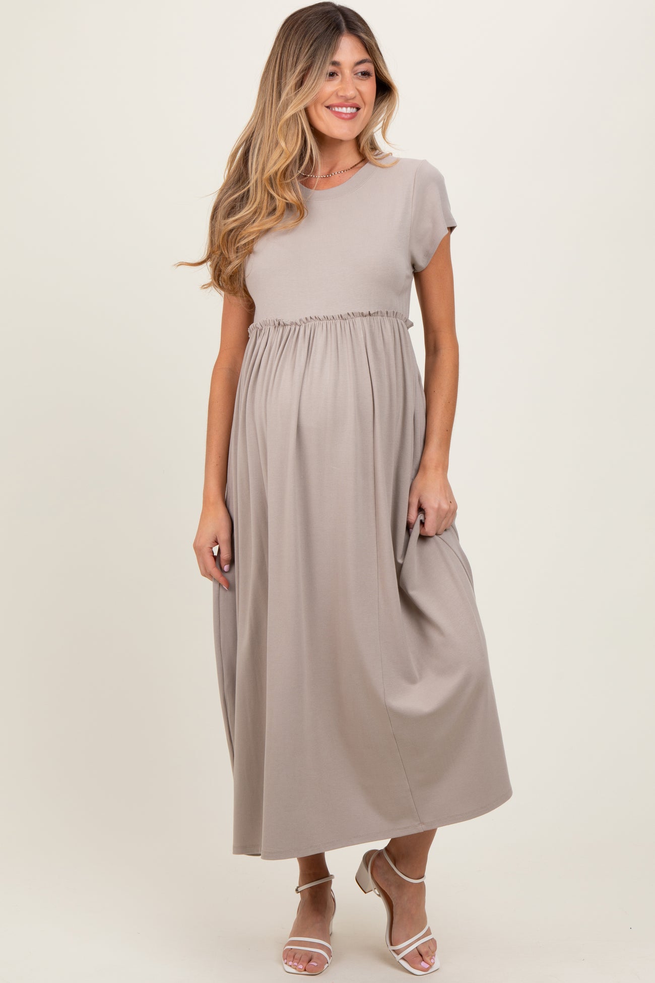 woman wearing a beige short sleeve maternity maxi dress with an empire waist and holding her baby bump