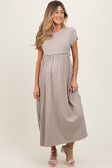 woman wearing a beige short sleeve maternity maxi dress with an empire waist and holding her baby bump