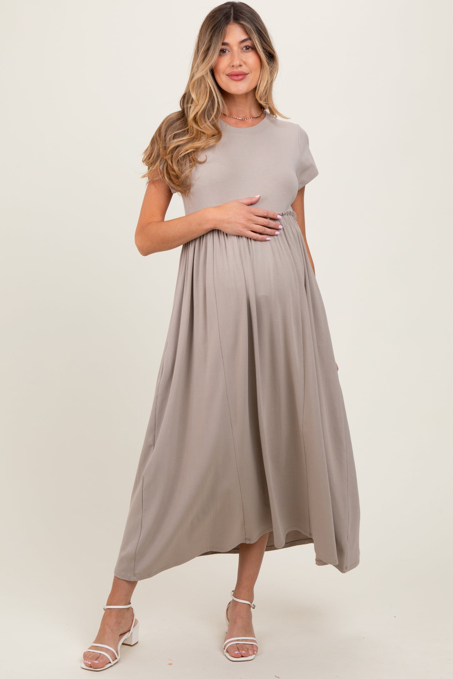 woman wearing a taupe short sleeve maternity dress with a flowing silhouette and holding her baby bump