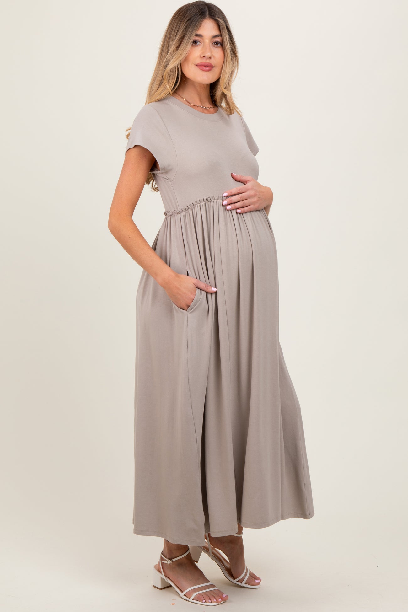 woman wearing a light taupe short sleeve maternity maxi dress with pockets and holding her baby bump