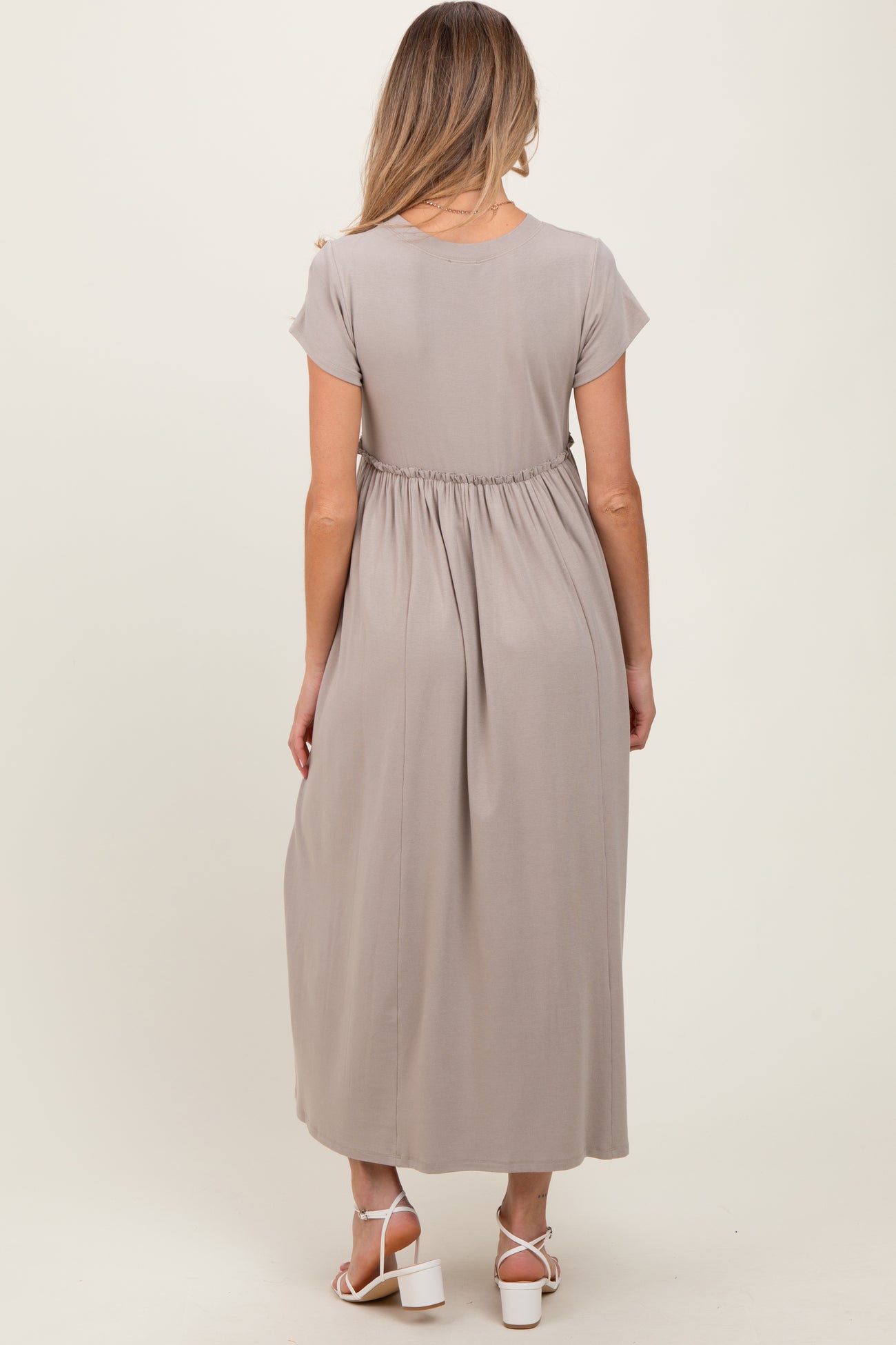 woman wearing a taupe maternity maxi dress with a gathered waist and short sleeves, view from the back