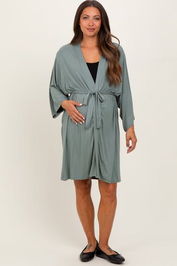 woman wearing a sage green maternity robe with a tie waist, gently holding her baby bump