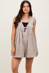 woman wearing a beige sleeveless playsuit with a v-neckline and tie detail, styled with a black top underneath