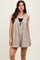 woman wearing a beige sleeveless playsuit with a v-neckline and tie detail, styled with a black top underneath