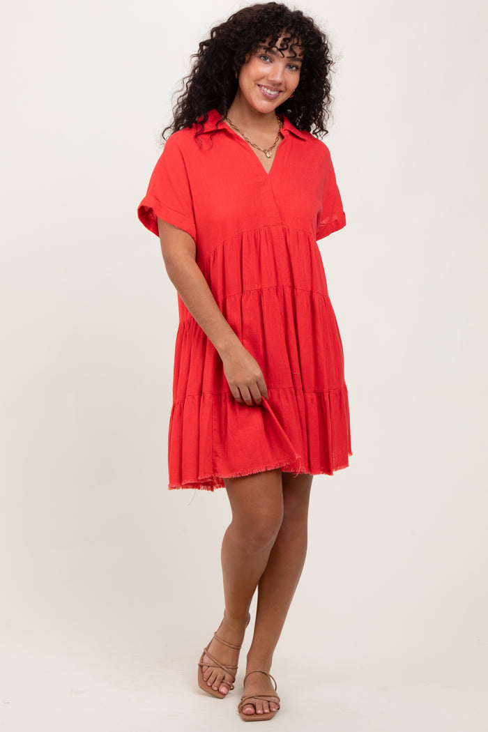 woman wearing a red tiered short sleeve dress with a collar and frayed hem, standing with one hand on her dress