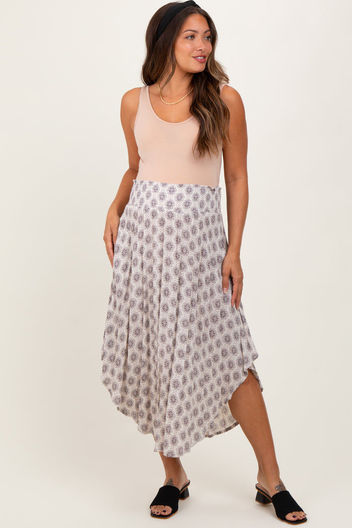 woman wearing a blush sleeveless top and a patterned maternity maxi skirt, styled with black slip-on shoes