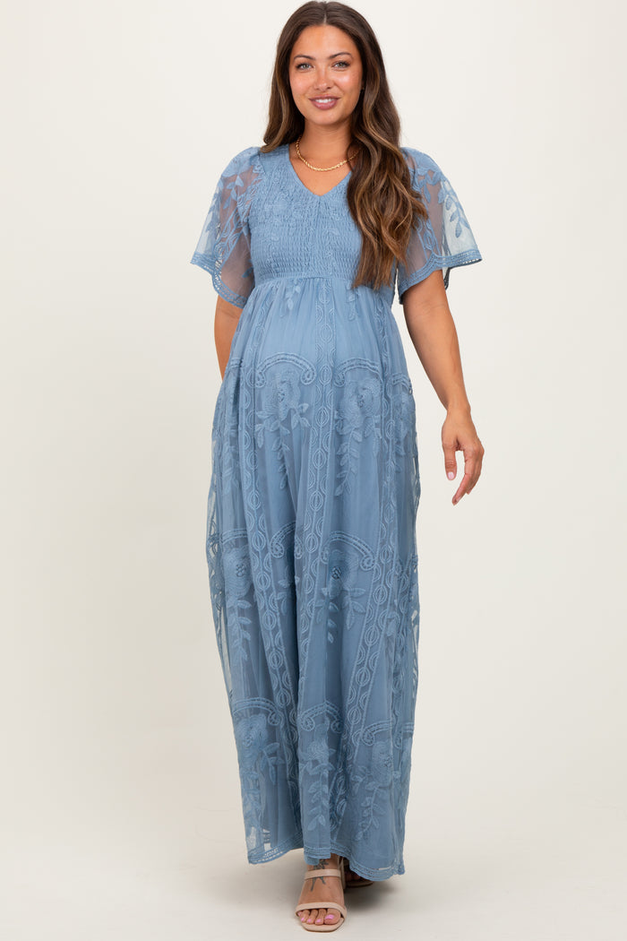 woman wearing a blue floral lace maternity maxi dress with short flutter sleeves and a visible baby bump
