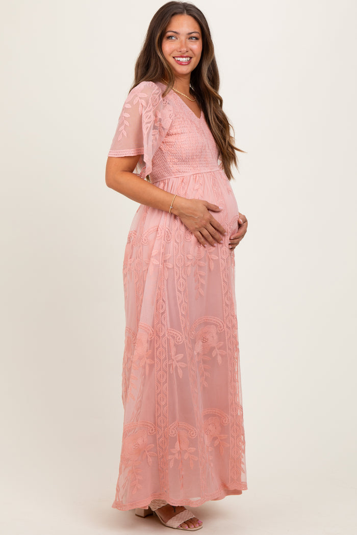 woman wearing a pink embroidered maternity dress with short sleeves and a flowing skirt, holding her baby bump